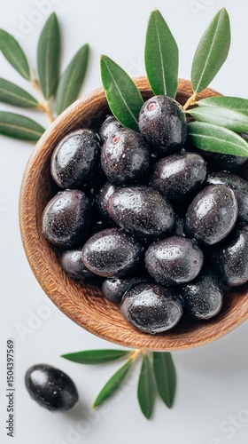 Black Olives in a Wooden Bowl With Fresh Leaves Displayed on a White Background