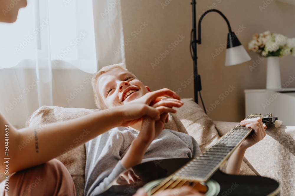 Obraz premium Mother and son playing guitar together, family love. The child wears a hearing aid, highlighting inclusivity and the universal language of music. Authentic, unedited photo captures emotions