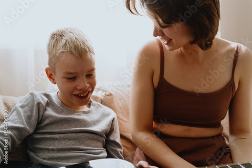 Mother and son playing guitar together, family love. The child wears a hearing aid, highlighting inclusivity and the universal language of music. Authentic, unedited photo captures emotions