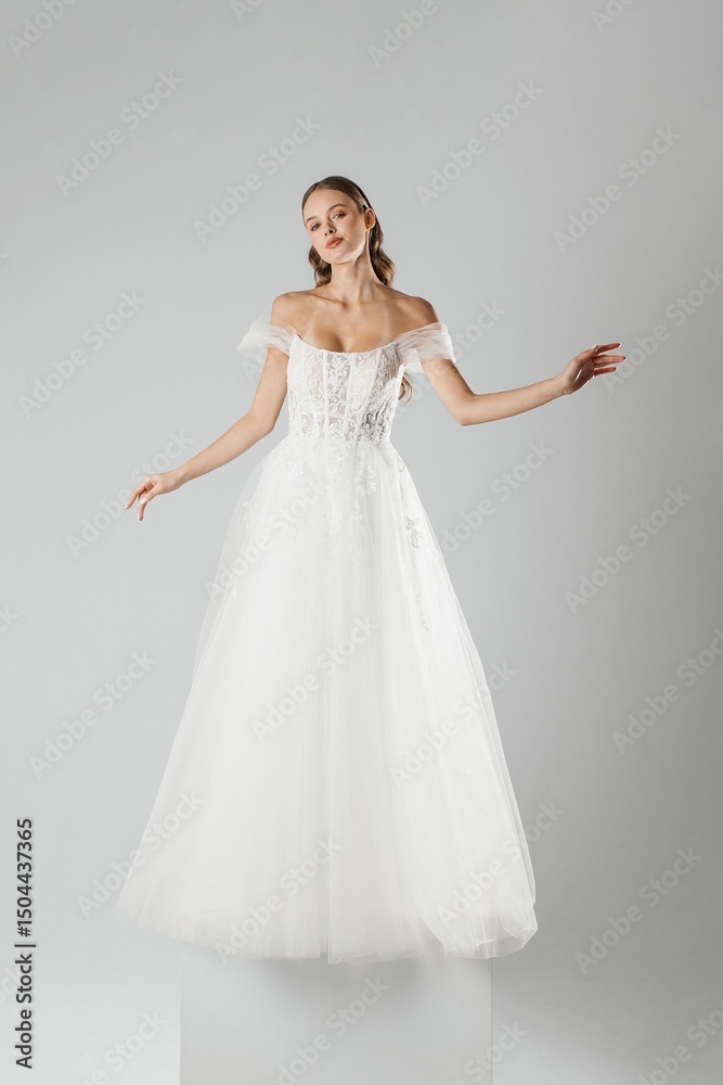 Fototapeta premium Stylish model showcases elegant white wedding dress in minimalist studio setting during fashion presentation