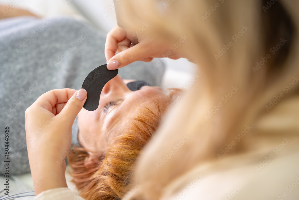 Naklejka premium Close-up of beautician hands holding black under-eye patch before UV eyelash extension. Professional tools preparation for modern lash enhancement technique.