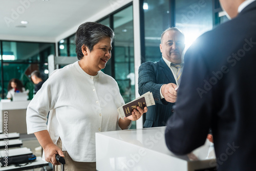 Senior Traveler at Airport Check-In Counter for Vacation Trip with Smiling Asian Elderly Woman in White Shirt photo