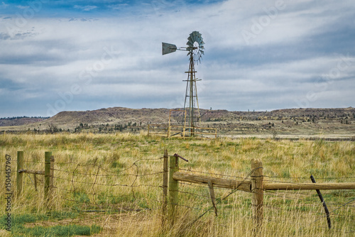 A windmill and barbed wire fence in the Montana landscape.