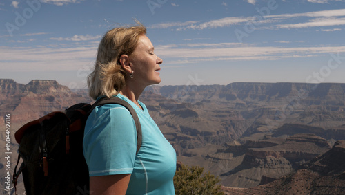 Adult caucasian mature woman hiker with backpack at top of Grand Canyon national park, enjoying view and success, slow breathe clean desert air full breasts, closes her eyes with pleasure and exhales