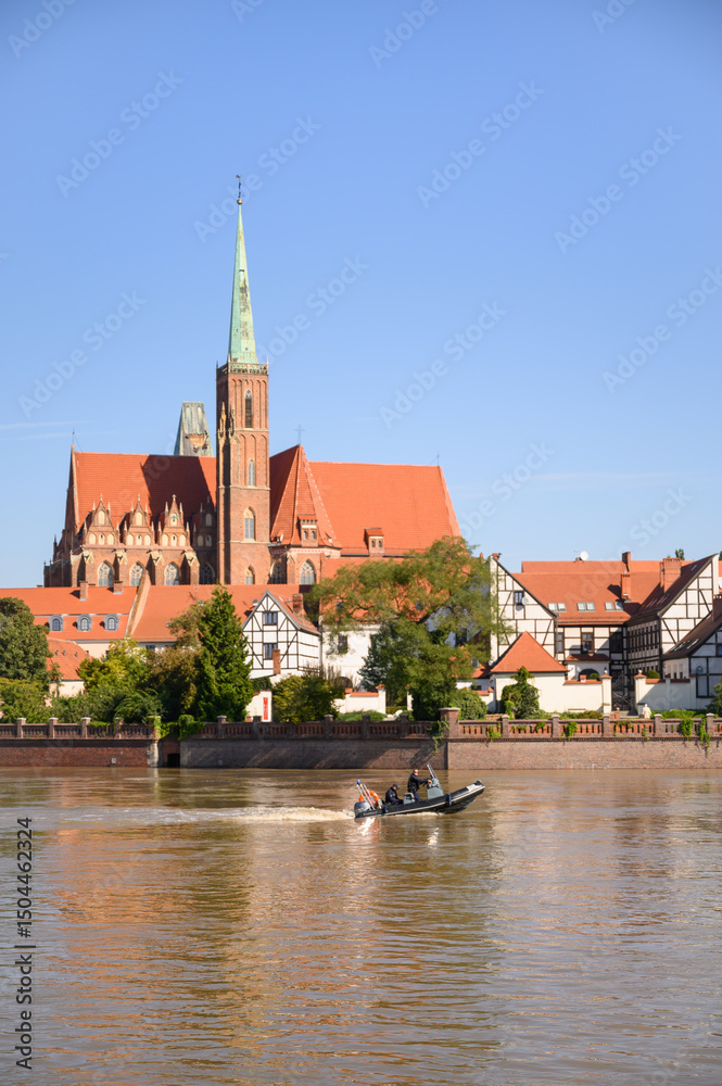 Obraz premium Wroclaw, Poland, September 21, 2024 — Emergency services patrol the flooded Oder River by motorboat near the Cathedral of St. John the Baptist, amid rising water levels threatening city infrastructure