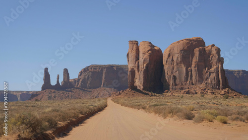 Driving car on dust road in dry hot desert with snags in monument valley in wild west of United States national park. High rock outcrop massifs of red and orange sandstone buttes destroyed by erosion.