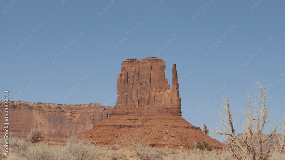 Fototapeta premium Shot in movement through dry hot desert with snags in monument valley in wild west of United States. Huge rock outcrop massifs of red and orange sandstone buttes destroyed by erosion.