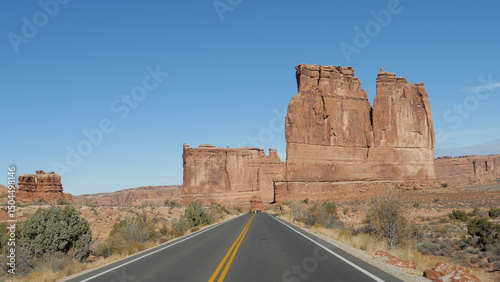 Driving on empty road in high rock buttes monument monolith of red orange sandstone hot desert, Arches national park in Utah Usa on sunny day. Pov in movement from riding vehicle car, slow motion.