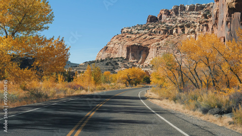 Driving on empty mountain highway with yellow markings on asphalt. Autumn sunny day, fall trees bright yellow golden foliage. Slow motion, view from riding vehicle car, transport delivery goods