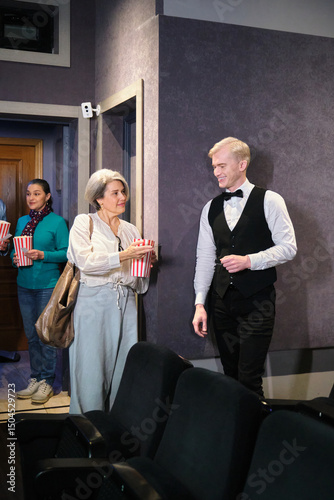 Foto Senior woman holding popcorn bucket and talking with cinema usher before enterin