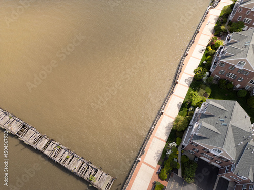 Aerial view of waterfront walkway bordering apartments and river with dilapidated pier. The waterway's color resembles silt or sediment stirred in the water. photo