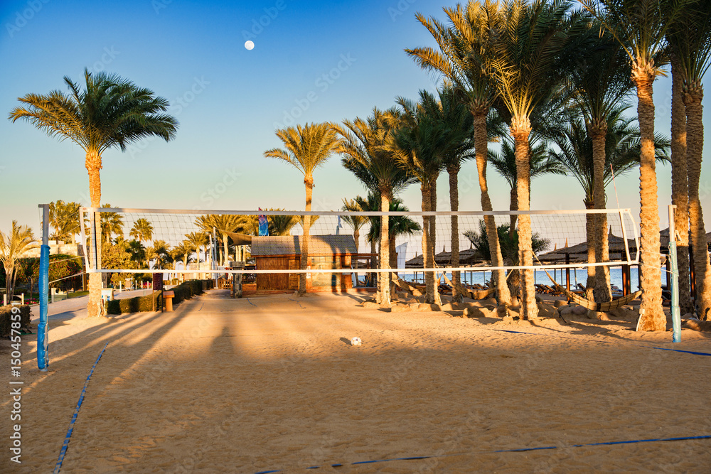 Obraz premium Volleyball court surrounded by palm trees and beach at sunset near tropical resort