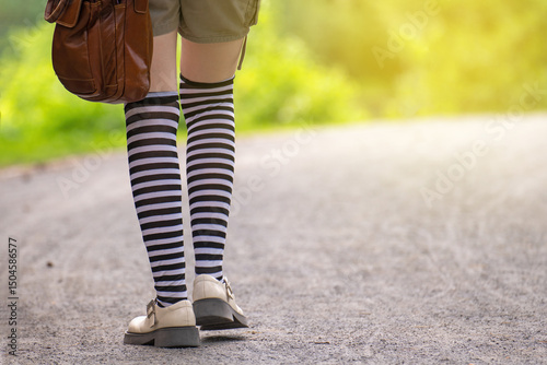Women's legs in high black-and-white striped stockings walking towards light, paired with an orange leather bag for a bold contrast