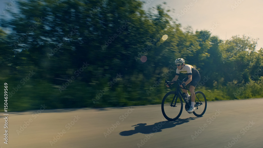 Obraz premium A helmeted cyclist rides down a scenic road, surrounded by lush greenery. The motion blur effect emphasizes speed and intensity. Aerial view.