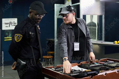 Security professionals discussing in control room with various equipment placed on table. One man demonstrating security gear while another observing and listening attentively