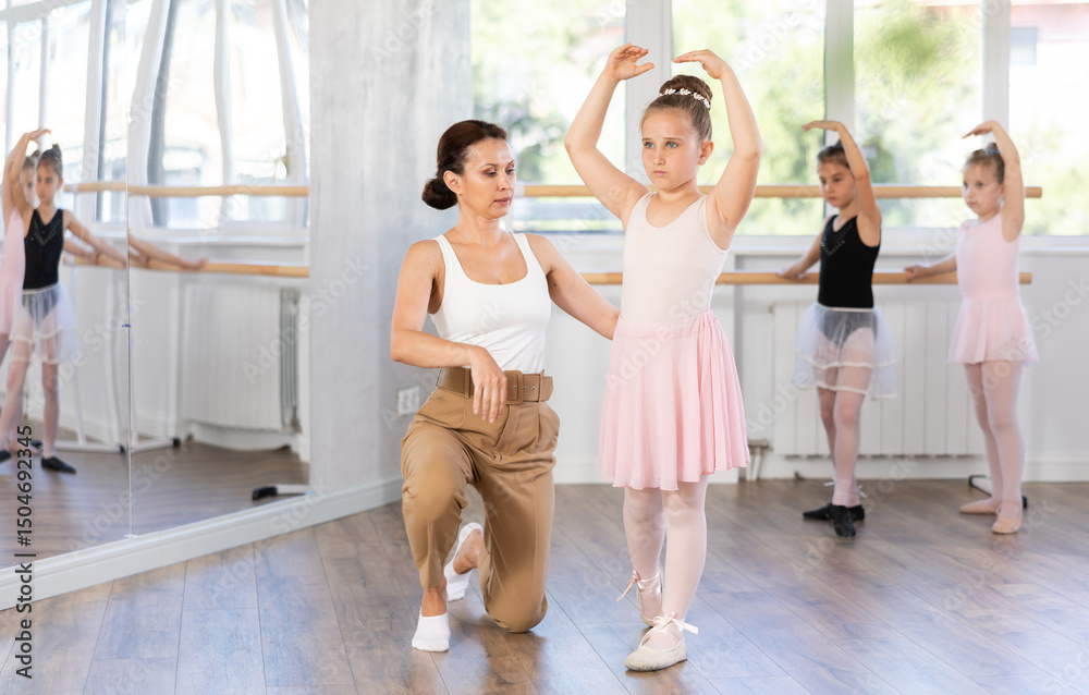 Obraz premium During classes at ballet school, mentor teaches how to hold pose legs and head correctly. Leader of studio corrects posture of students girl, helps to learn holding leg and arm correctly during figure
