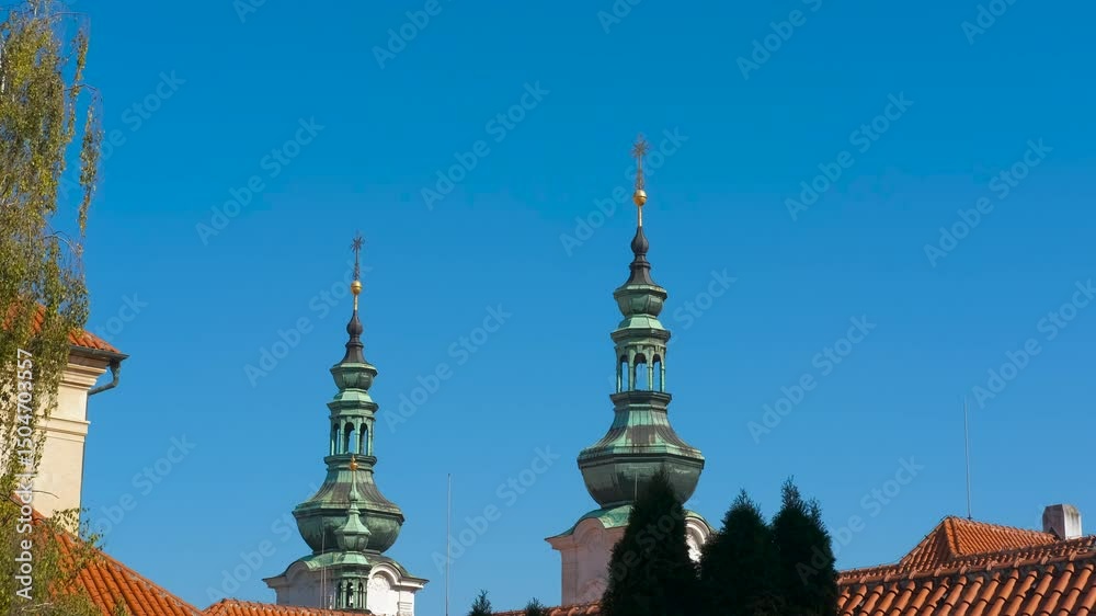 Majestic church towers reaching for a vibrant blue sky. Sunlight casting vibrant colors on historic church's green oxidized copper domes, complemented by red tile roofs