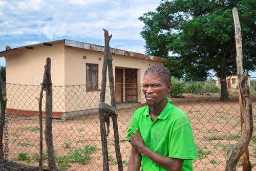 african village single smiling young african man, in front of house , typical home with wire fencing , rural living