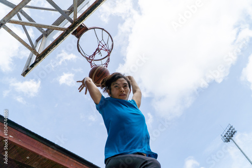 Denpasar, 13 Feb 23: A young athlete performs a slam dunk at a street basketball court under the midday sun in Bali, Indonesia.