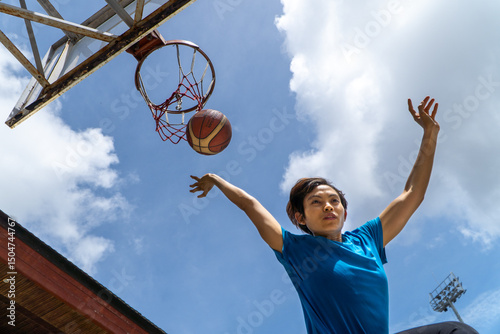 Denpasar, 13 Feb 23: A young athlete performs a slam dunk at a street basketball court under the midday sun in Bali, Indonesia.