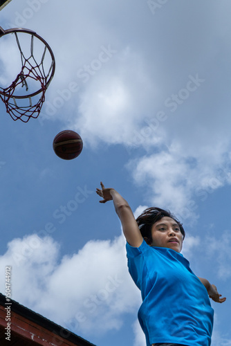 Denpasar, 13 Feb 23: A young athlete performs a slam dunk at a street basketball court under the midday sun in Bali, Indonesia.
