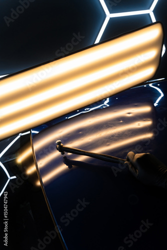Fototapete PDR technician holds a specialized hammer against a reflection light board to check dent correction on the hood