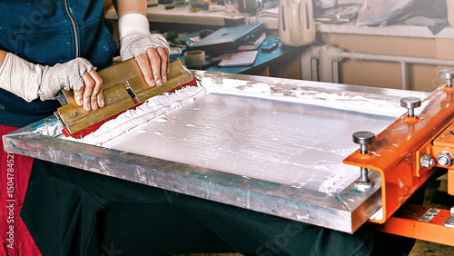 silk screen textile printery. manual screen printing. selective focus photo of male hands with a squeegee