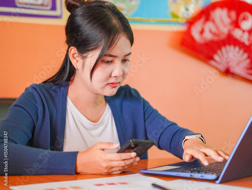 Fotografie Asian businesswoman using smartphone, laptop, researching about startup business or small business