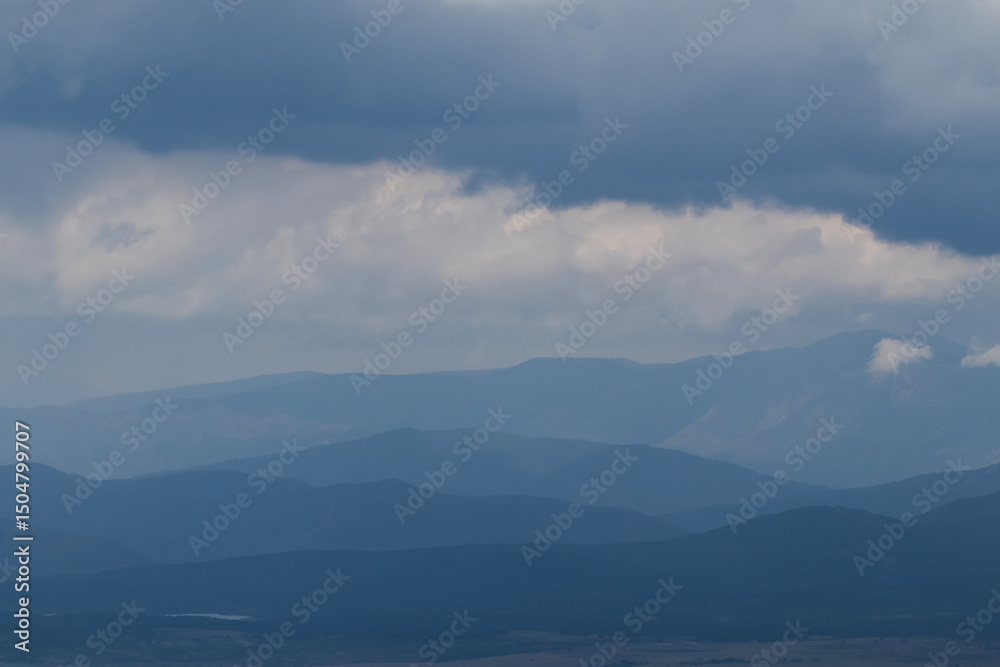 Obraz premium Lines of mountains on the horizon, gradually fading into soft blue tones under a cloudy sky