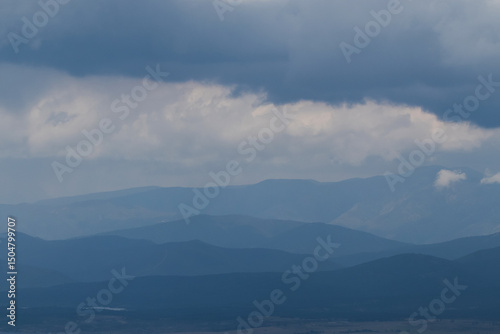 Lines of mountains on the horizon, gradually fading into soft blue tones under a cloudy sky