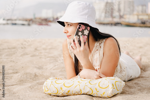 A woman is laying on the beach and talking on her cell phone