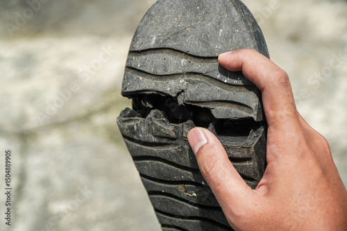 Close-up capturing a worn-out shoe sole held by a hand, emphasizing wear and tear. The damaged rubber textures highlight material degradation and the need for replacement footwear or repair services.