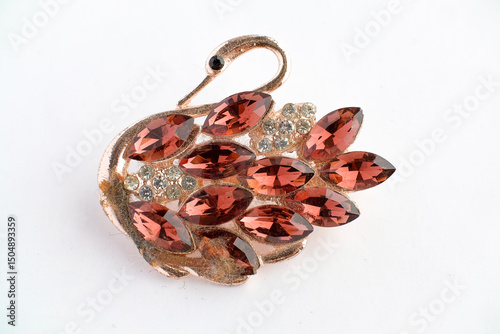 Close-up image of a decorative brooch shaped like a swan, adorned with marquise-cut red gemstones and round clear crystals on a gold-tone base. Photographed on a white background.