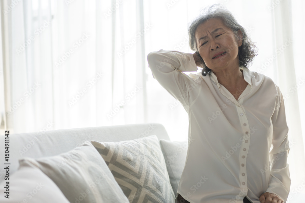 Asian senior woman suffering from neck pain while sitting on sofa showing signs of muscle inflammation, common elderly health issues, office syndrome, physical therapy, senior care and muscle strain Asian senior woman suffering from neck pain while sitting on sofa showing signs of muscle inflammation, common elderly health issues, office syndrome, physical therapy, senior care and muscle strain