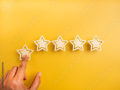 Five wooden stars ratings, pointing by customer hand, on yellow background. 5 points, highest level of excellence quality or satisfaction, customer evaluation ranking, business marketing concept.