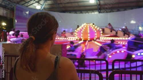 Wallpaper Mural Nighttime carousel spinning, vibrant lights glowing, woman watching from behind, experiencing magical amusement park moment Torontodigital.ca
