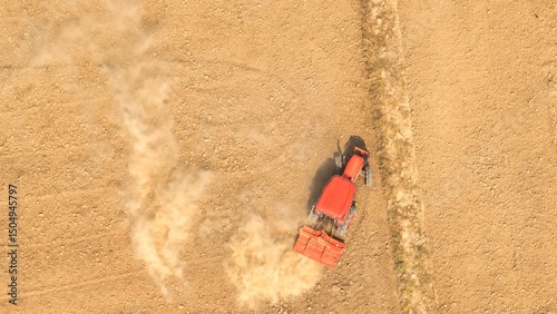 Photography A crimson tractor, adorned with a cultivator, cuts through the dusty terrain, breathing vigor into the desolate vista