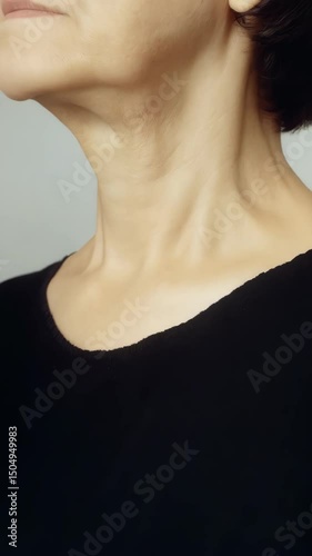 Close-up of neck and collarbone of a fair-skinned woman, showing signs of aging with some wrinkles and sagging skin wearing a black sweater
