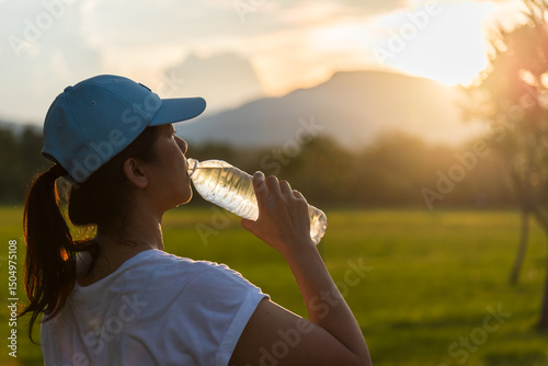 Asian woman drinking water after running and training outdoors at sunset. Healthy girl drinking water from bottle for outdoor exercise, running workout or fitness training concept.