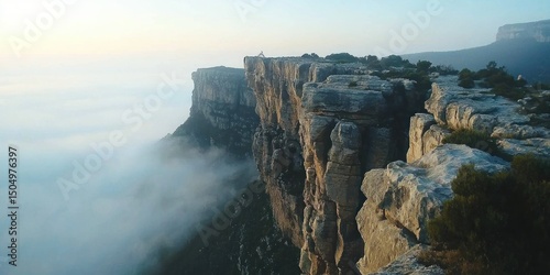 A rugged mountaintop with sheer cliffs dropping into a misty canyon below
