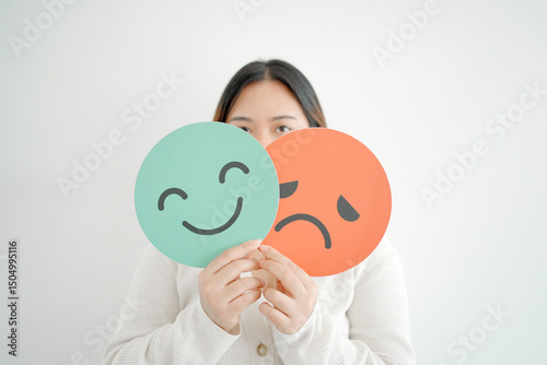 Woman hands holding sad face hiding behind happy face, bipolar and depression, mental health, split personality, mood change concept
