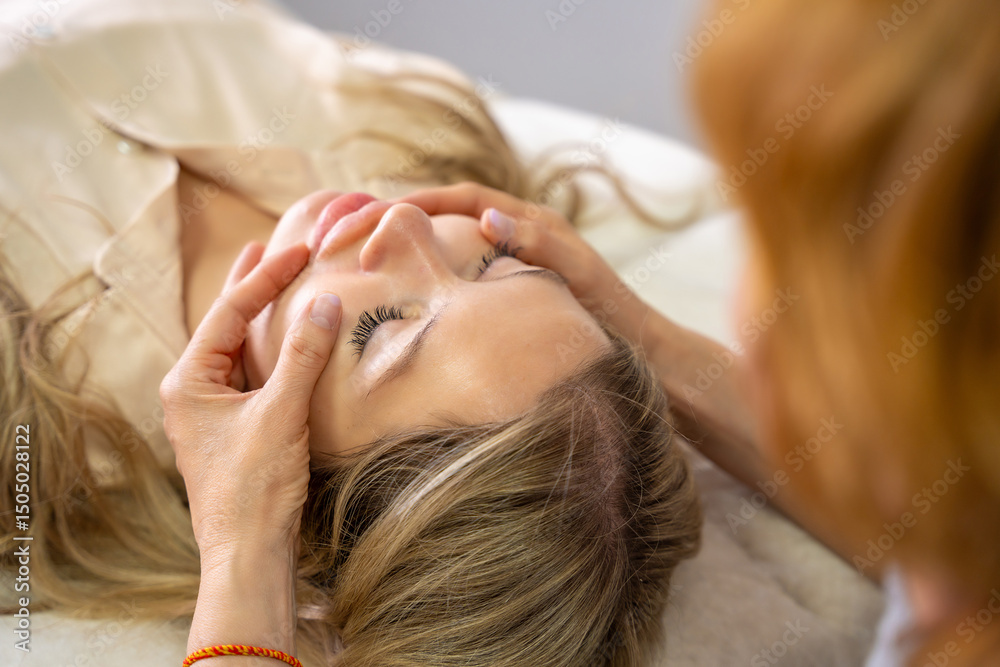 Fototapeta premium Hands of a female practitioner positioned on the face of a young woman during an Access Bars facial lifting session. Concept of energy work, healing touch and alternative face therapy