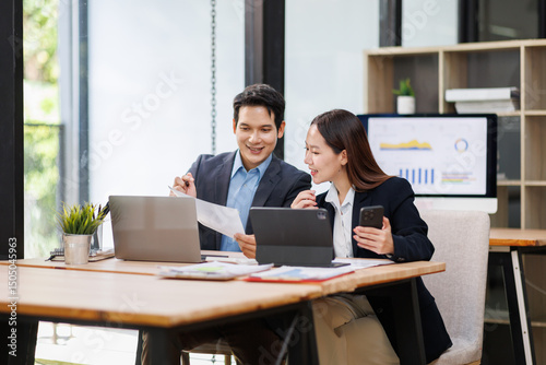 Young Asian Man and Woman manager project on laptop in modern office. Two business people of professional working, studying, writing notes sit at desk 
