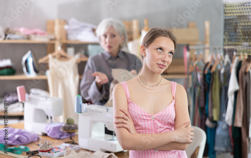 Mature dressmaker scolds assistant with displeasure at work in a sewing workshop. Head of the sewing production is dissatisfied with the young seamstress and reprimands her photo