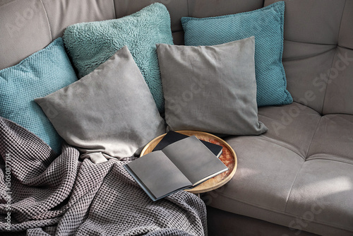 Open Book on Round Tray Rests on a Gray Sofa Draped with Soft Blanket. A Cozy Living Room Scene.