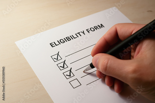 A person is checking boxes on an eligibility form with a pen on a light wooden surface.