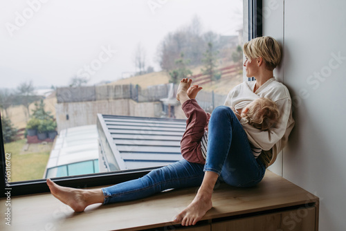 Mother breastfeeding her toddler son by the window
