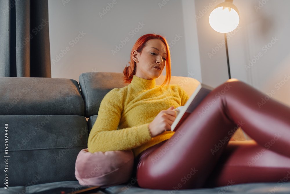 Obraz premium Woman relaxing on sofa reading a book and drinking tea