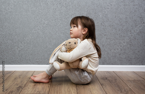 Konstfotografi Sad child sits alone near the wall and hugs a teddy bunny