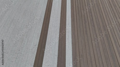 slow-motion drone shot reveals perfectly parallel strips of pale tilth and rich brown earth freshly leveled across a vast field forming an orderly grid poised for the next planting season